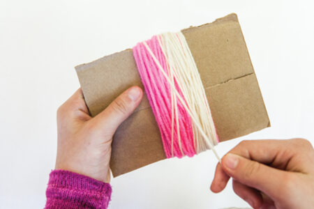person wrapping white yarn around pink yarn on cardboard
